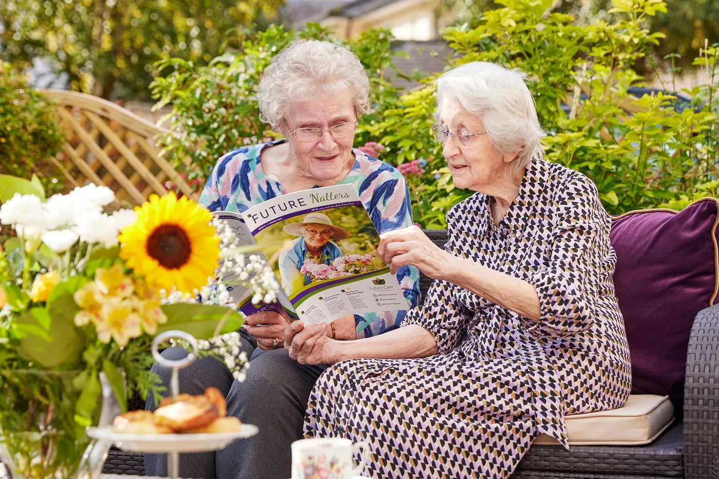 Two Future Care Group residents reading a magazine together in a garden