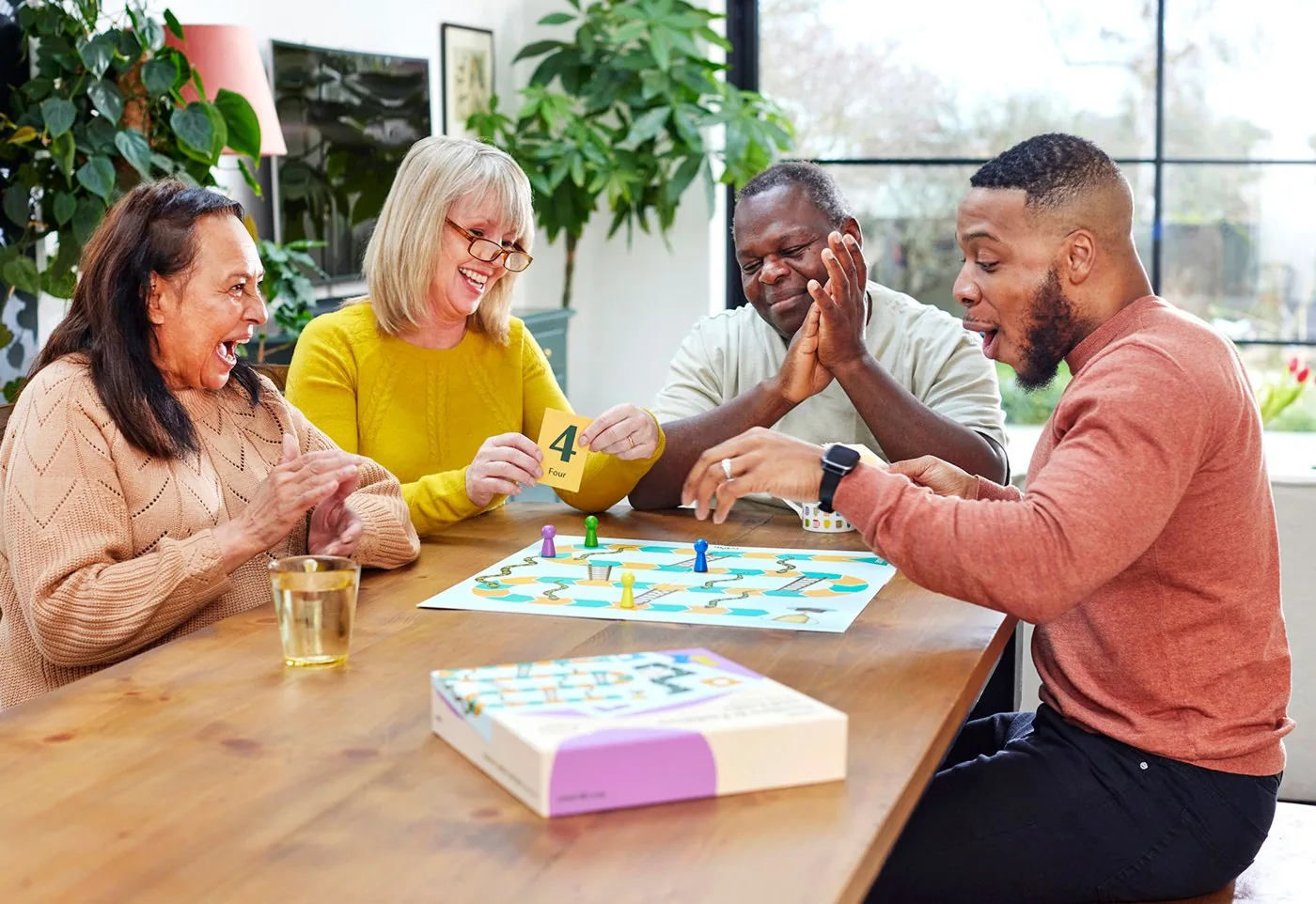 Four friends laughing around a table playing a Relish board game