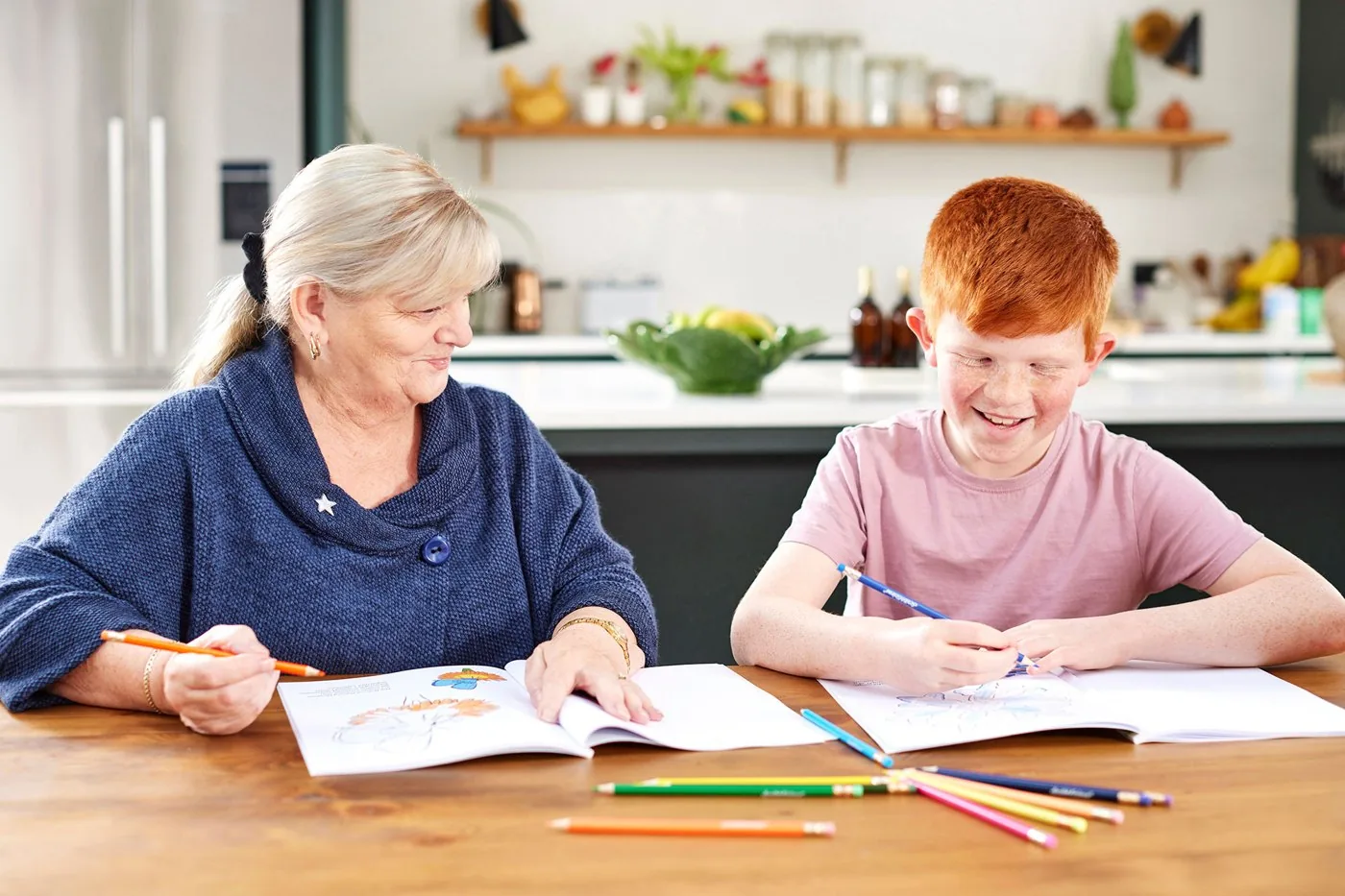 A grandmother and young boy drawing together at a kitchen table
